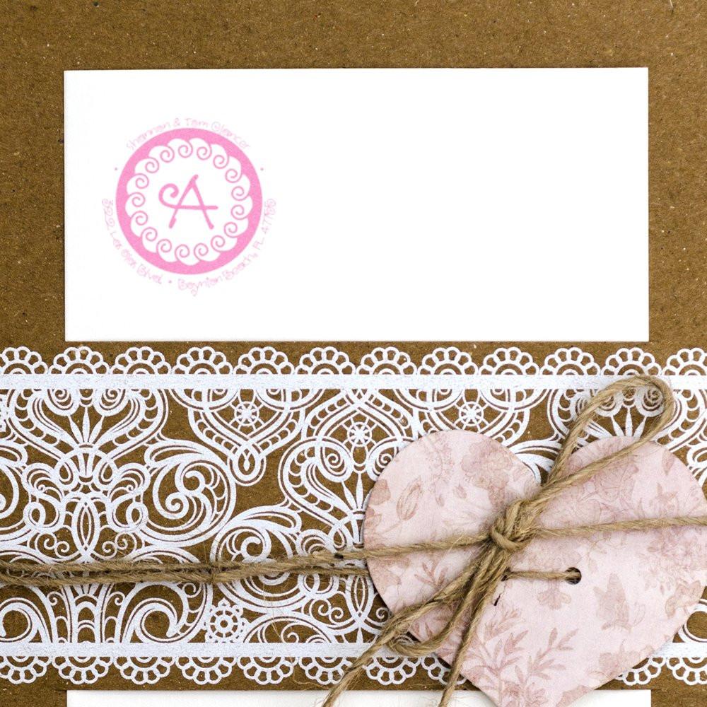Custom pink monogram rubber stamp on a wedding invitation envelope with lace trim and heart tag tied with twine.