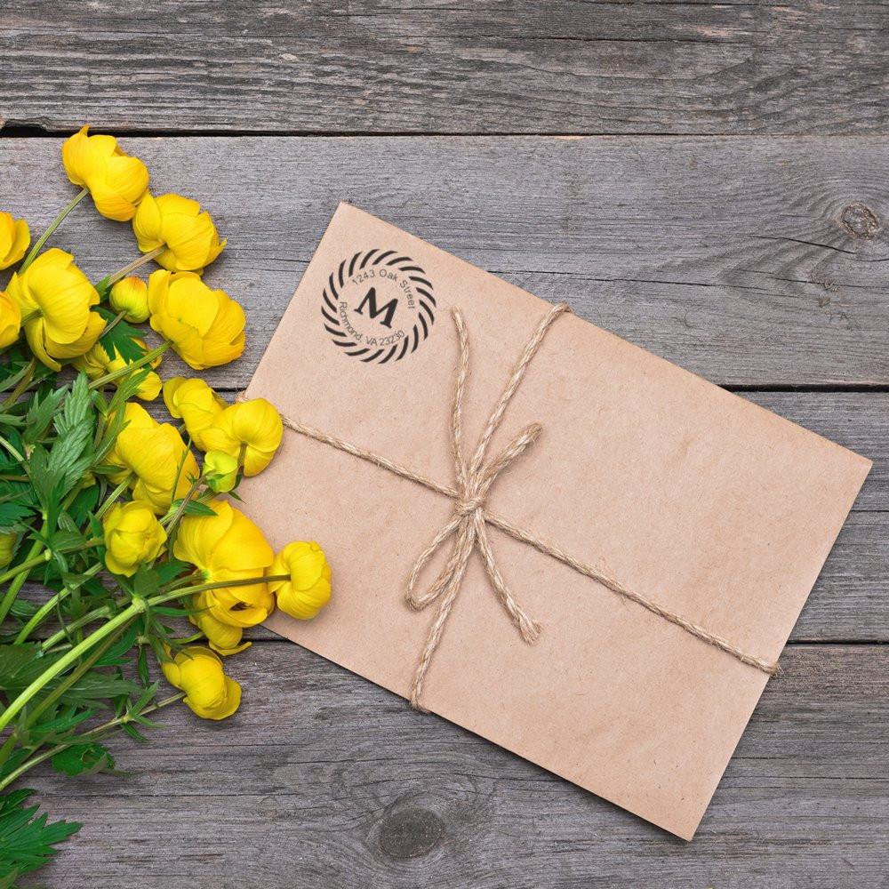 Kraft paper gift envelope with branded stamp tied in twine, next to yellow wildflowers on rustic wood for handmade wedding invitations