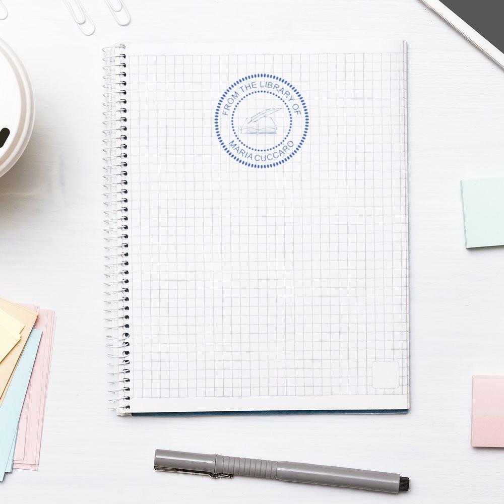 Custom rubber library stamp reading From the Library of Maria Cuccaro on a graph notebook.