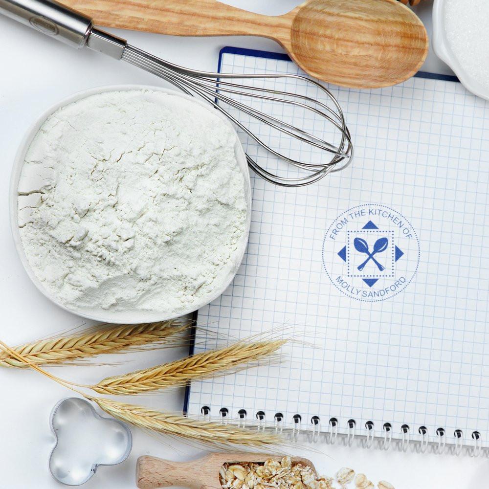 Personalized rubber stamp for recipes and baking, styled in a kitchen flat lay with flour, whisk, and notebook.