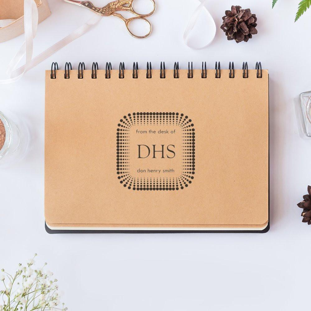 Custom rubber stamp on notebook for personalized office stationery, featuring a modern from the desk of monogram design.
