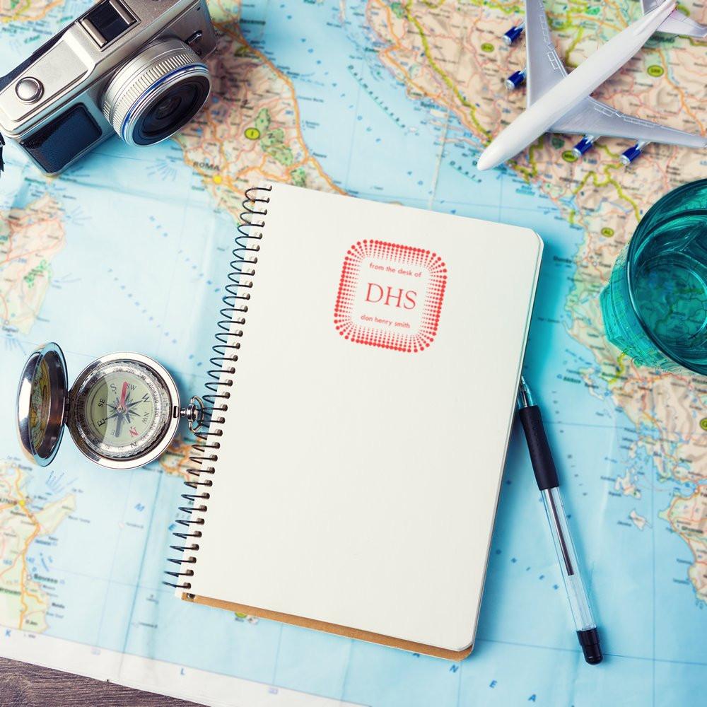 Custom rubber stamp mockup on travel notebook over world map with camera, compass and plane