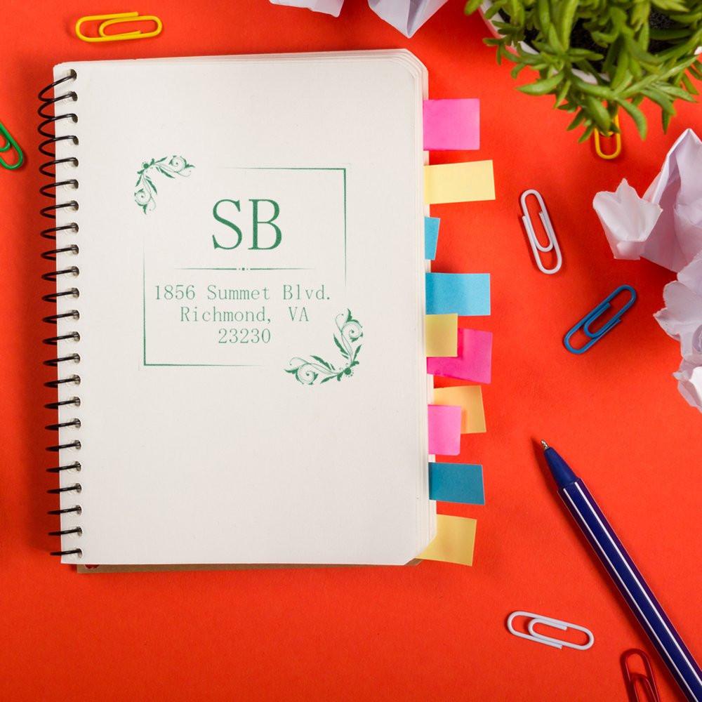 Custom return address rubber stamp impression on spiral notebook, featuring monogram design for personalized stationery and branding.
