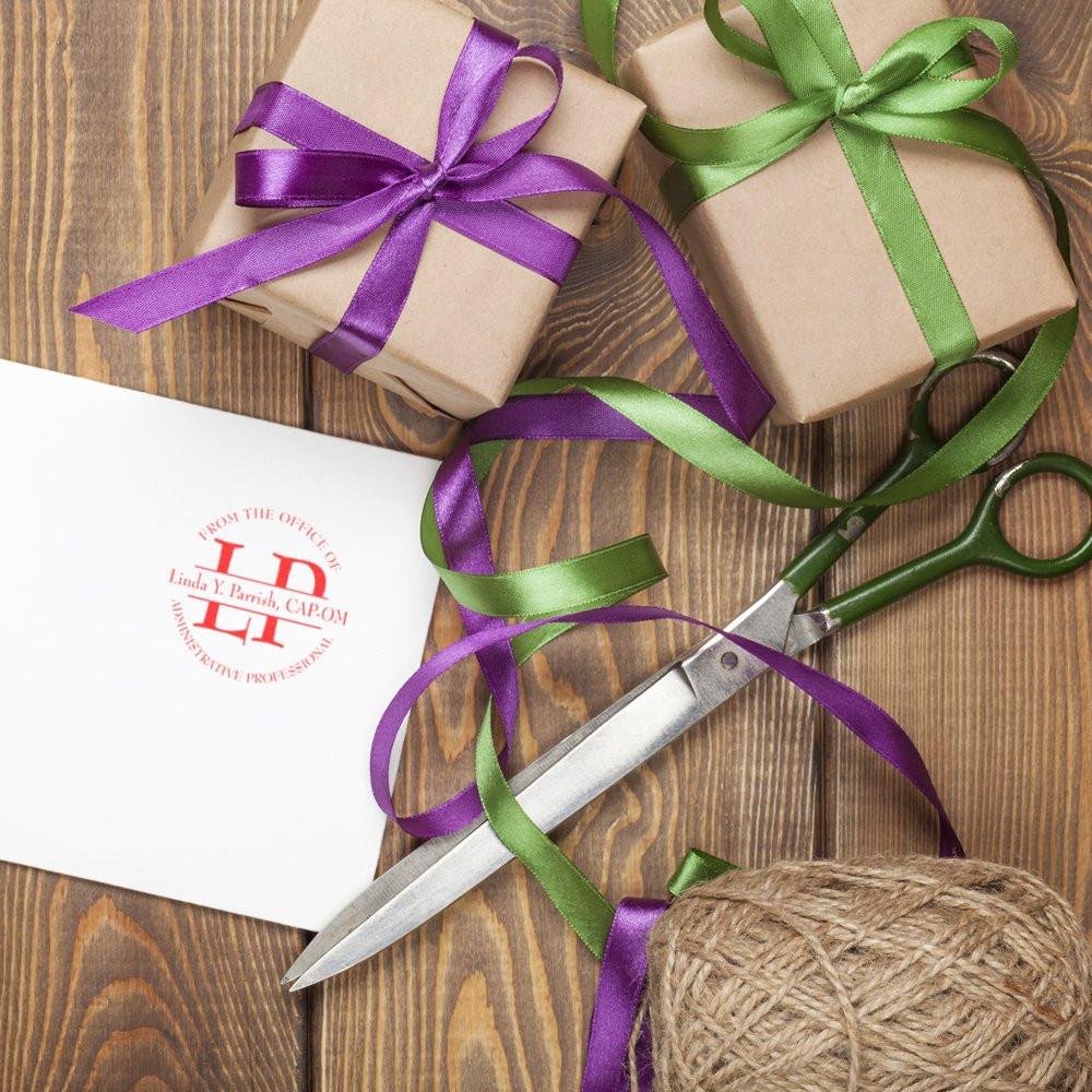 Custom rubber stamp on gift card beside wrapped presents, ribbon, scissors, and twine for creative gift wrapping.