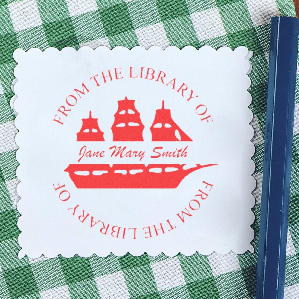 Personalized bookplate rubber stamp impression with red From the Library of design and custom name on white scalloped paper