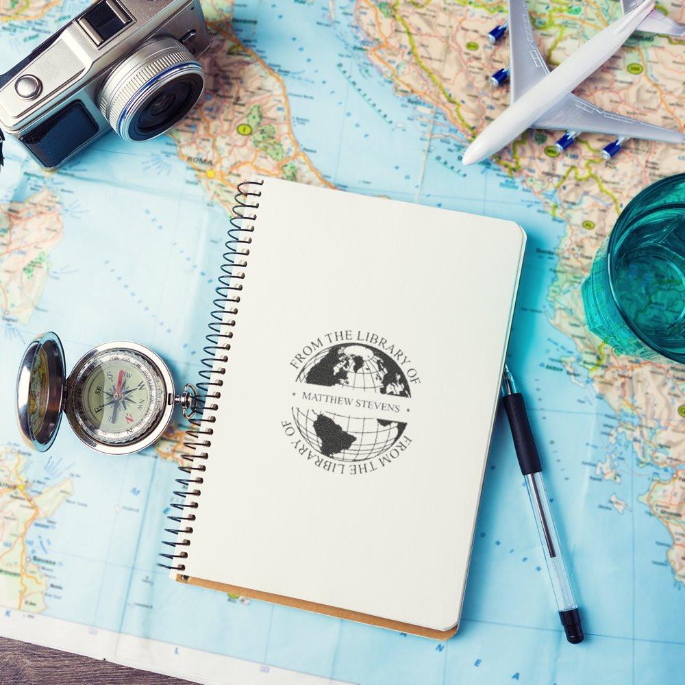 Custom library rubber stamp on notebook over a travel map, with compass, camera and plane for personalized book lovers
