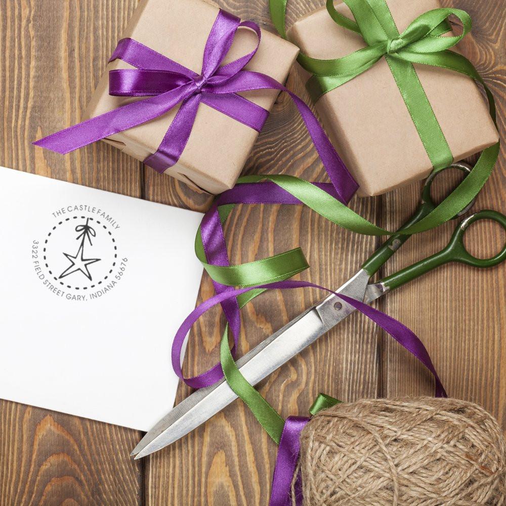 Personalized address rubber stamp for gift packaging, shown with wrapped presents, ribbon, scissors, and twine.