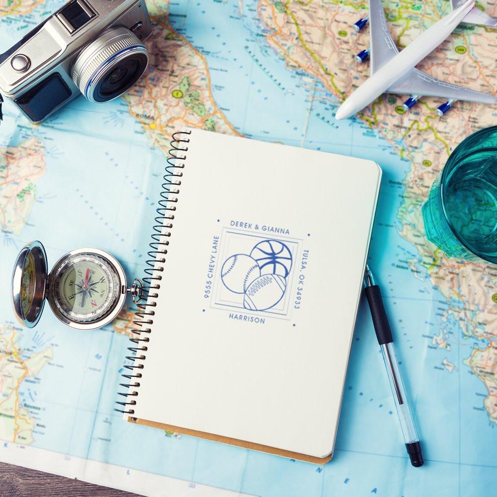 Custom travel address rubber stamp mockup on notebook with map, compass, camera and airplane for vacation journaling.