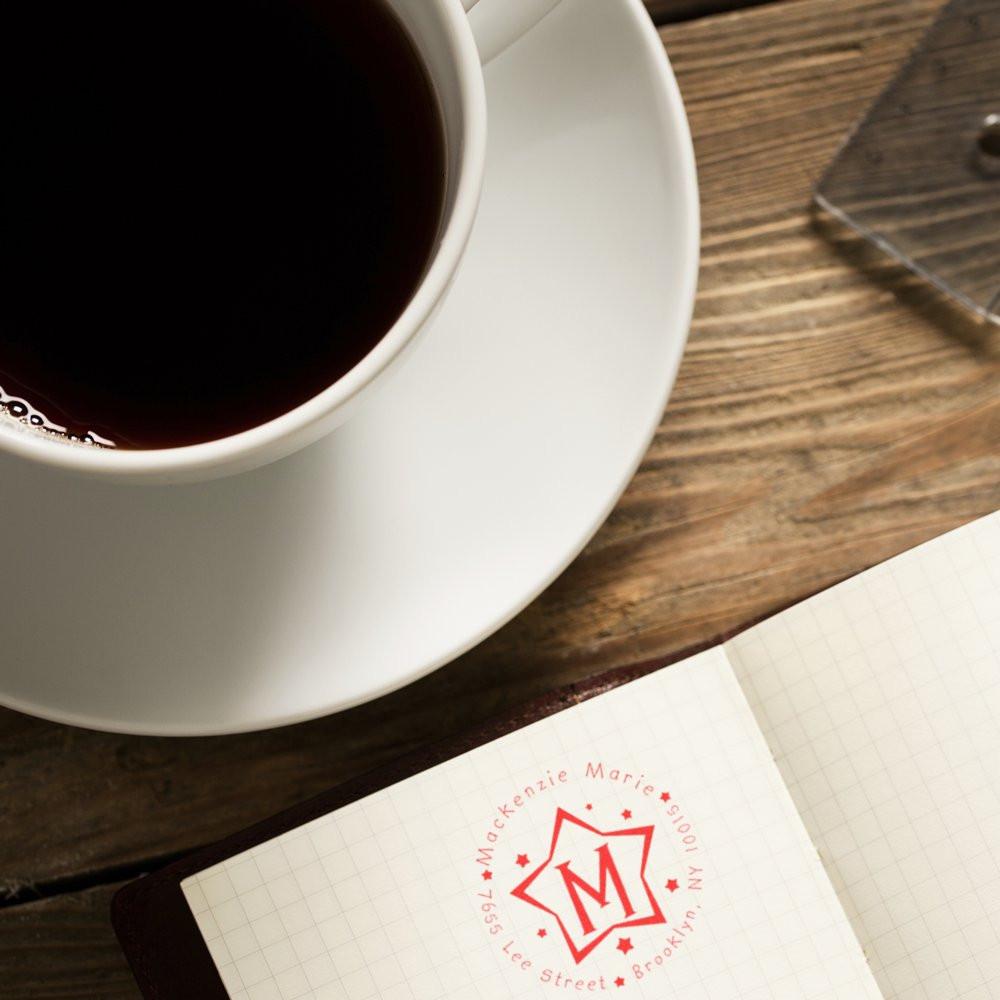 Black coffee cup beside notebook with red 'M' logo reading Mackenzie Marie's for Brooklyn caf branding and coffee lifestyle scene.