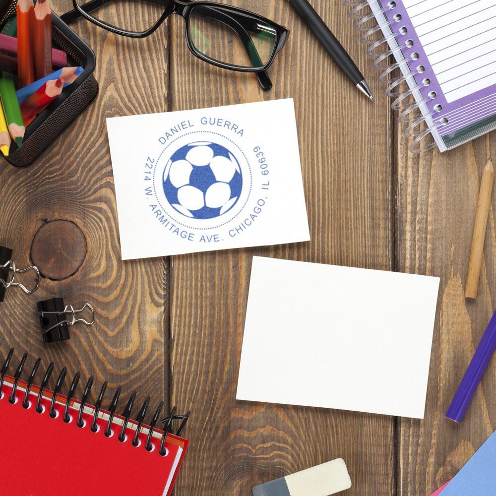 Custom return address rubber stamp with soccer logo on paper, displayed on a desk with stationery for business mailing.