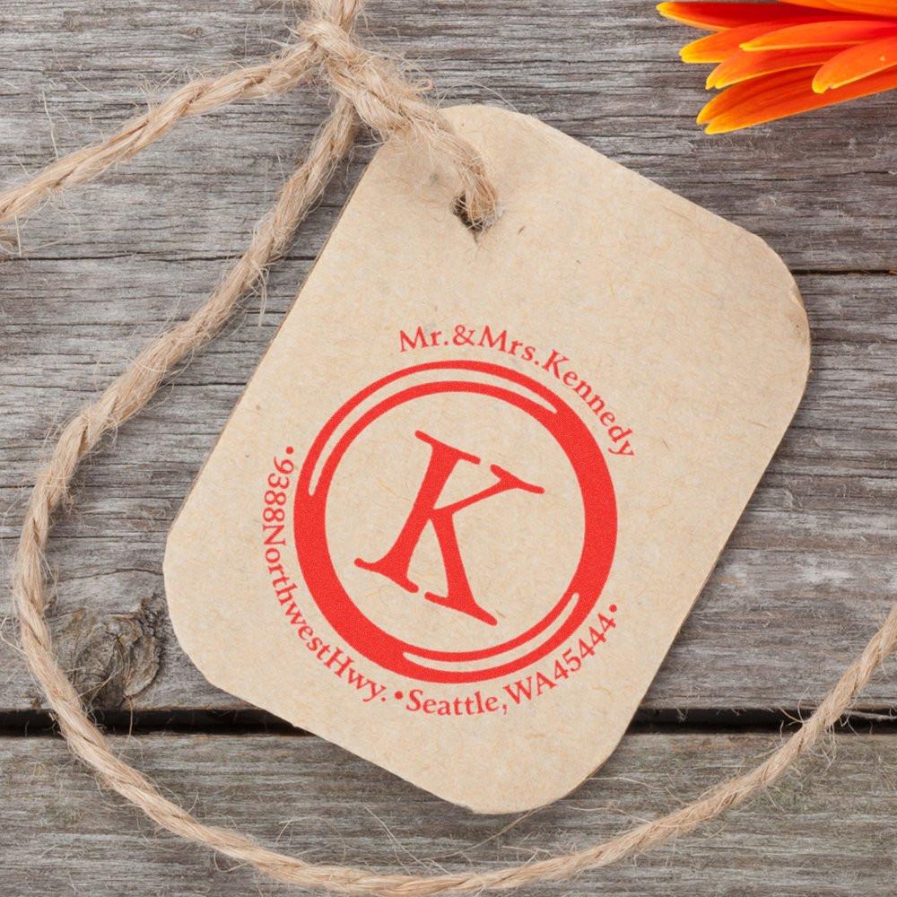 Custom wedding address tag on kraft paper with couple names, red monogram symbol, and Seattle WA contact details.