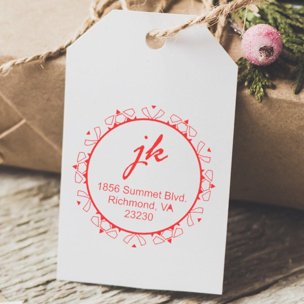 Custom rubber stamp return address on white gift tag for holiday packaging, featuring a red monogram and address design.