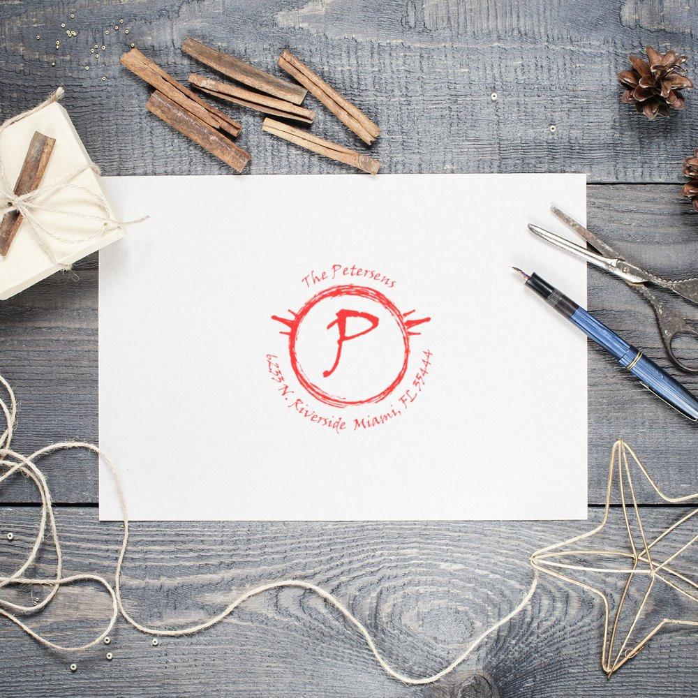 Custom monogram stationery card for The Petersens with red P seal, placed on rustic wood desk with pen and scissors.