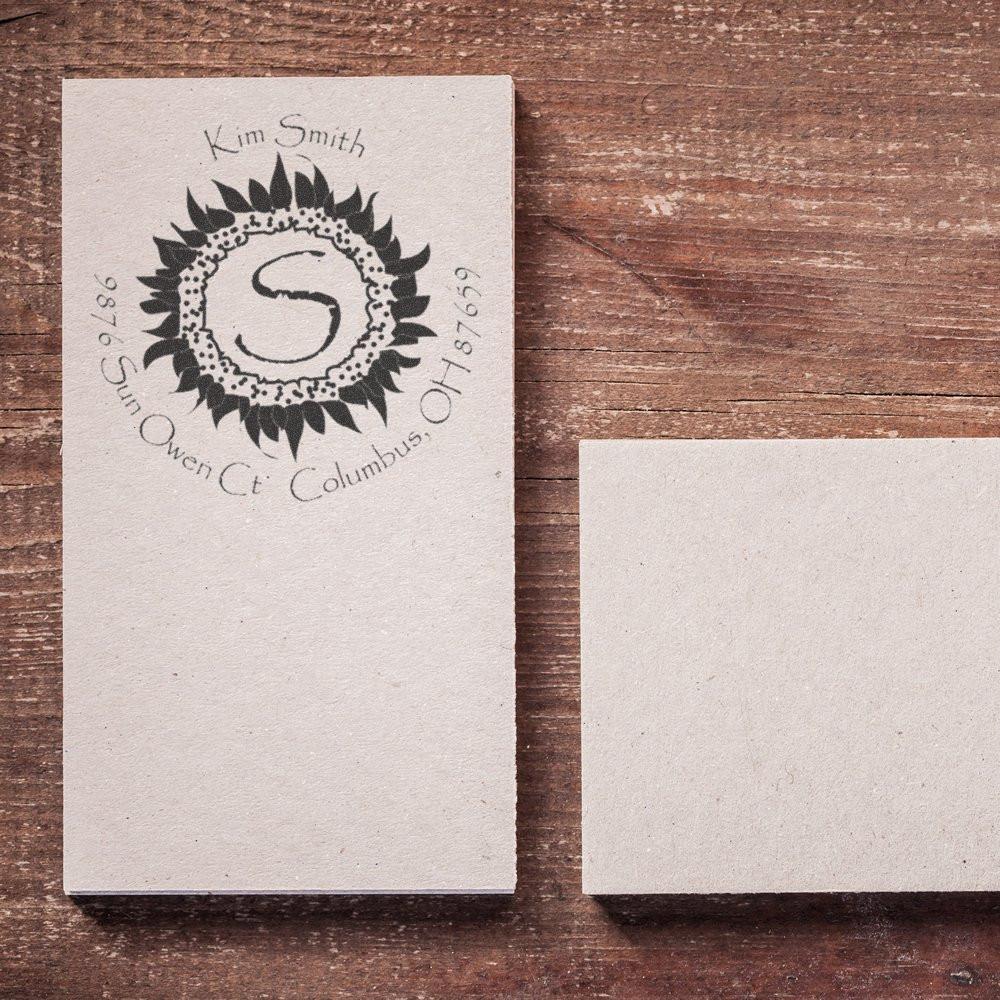 Custom rubber stamp sample with floral monogram, name, and address stamped on paper beside a blank card.