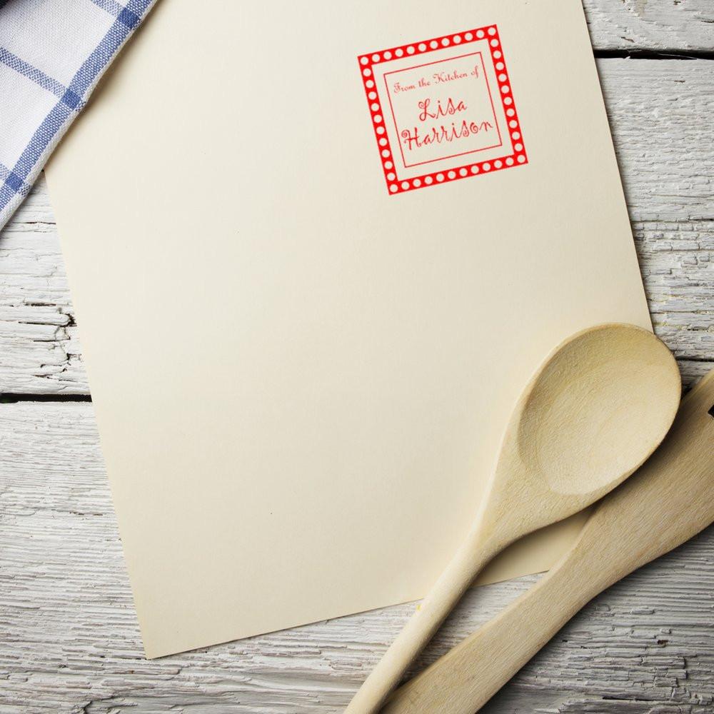 Personalized kitchen rubber stamp on cream paper with wooden spoons, featuring custom From the Kitchen of Lisa Harrison design.