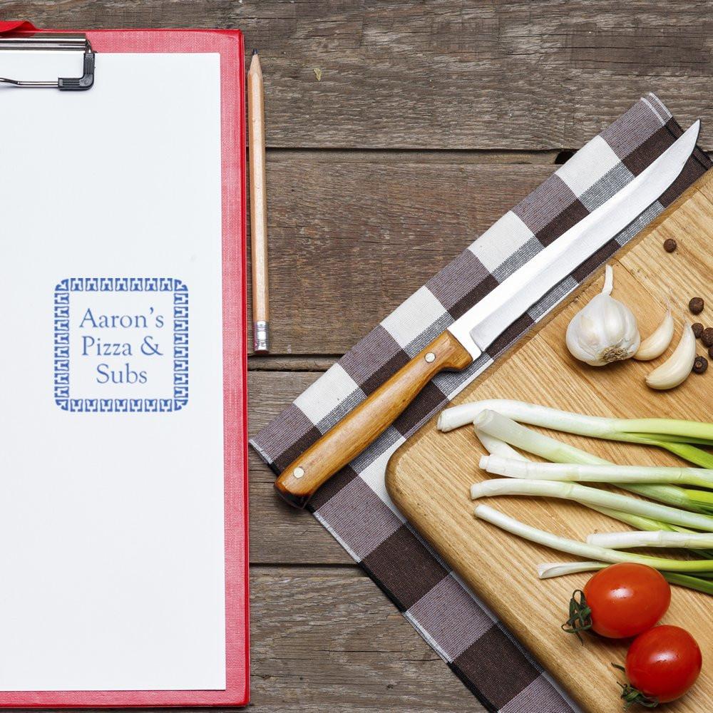 Custom restaurant logo rubber stamp for Aarons Pizza & Subs on a clipboard beside pizza prep ingredients.