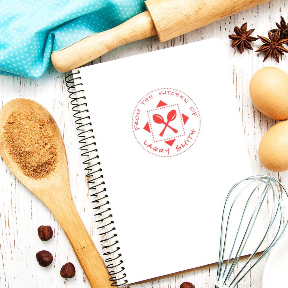 Custom kitchen rubber stamp on recipe notebook, with baking tools and whisk, ideal for culinary branding and recipe pages.