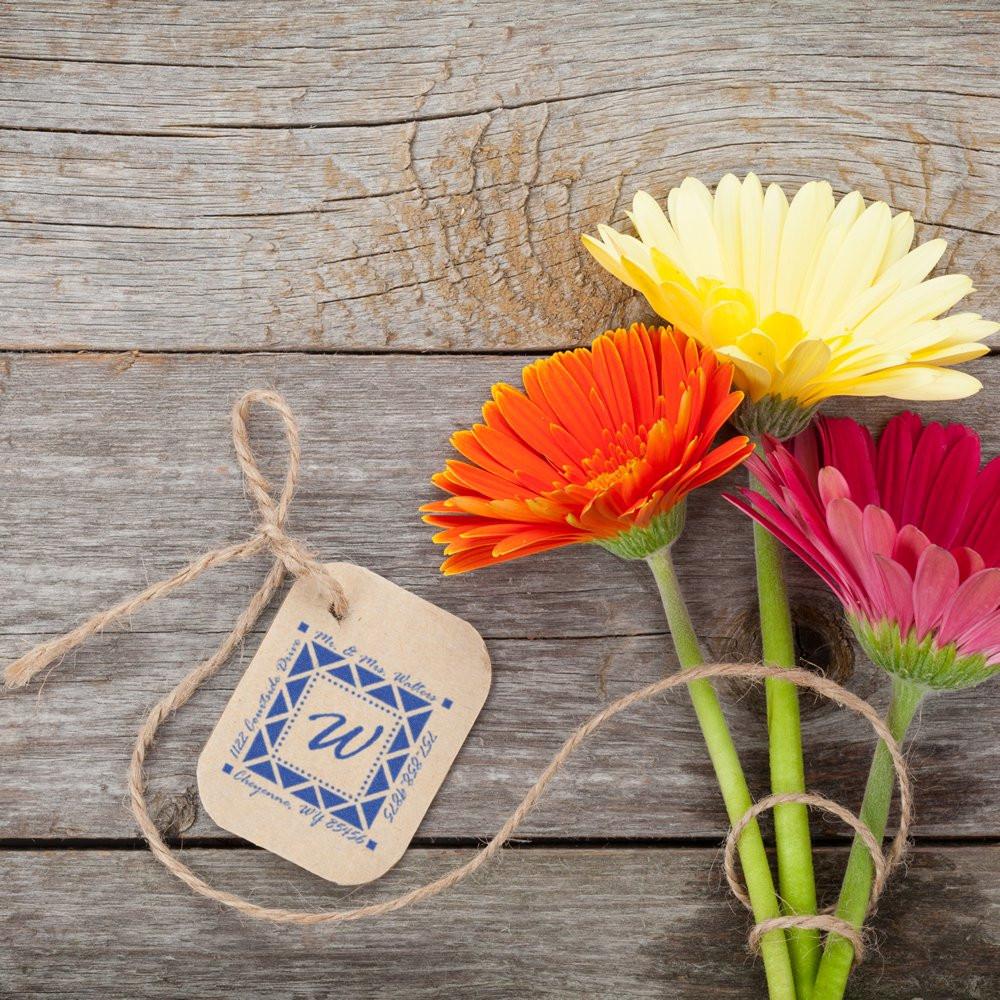 Personalized rubber stamp logo on kraft gift tag with twine and flowers, showing custom branding for rustic packaging.