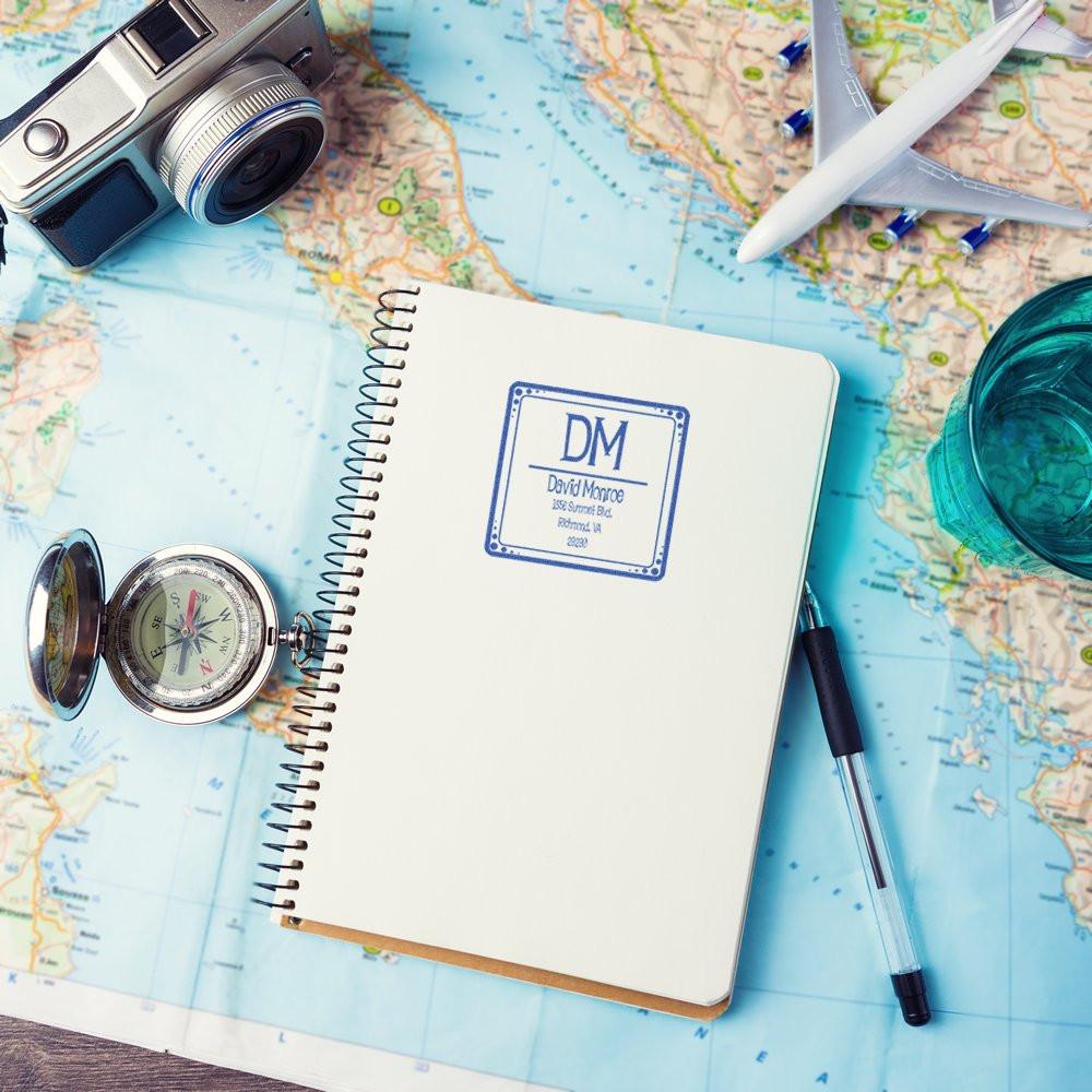 Custom rubber address stamp on travel journal notebook, with map, camera, compass and airplane for travel-themed branding.