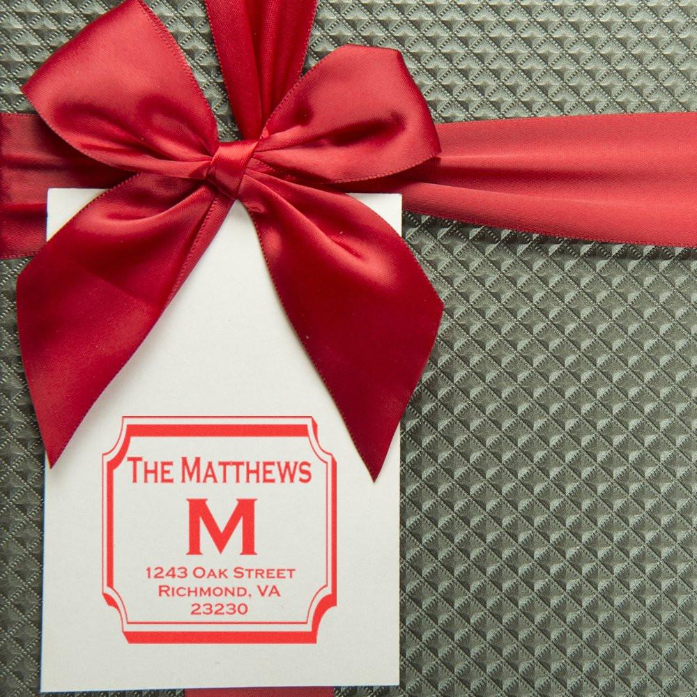 Custom monogram return address rubber stamp on a gift tag with red ribbon for personalized stationery or holiday packaging.