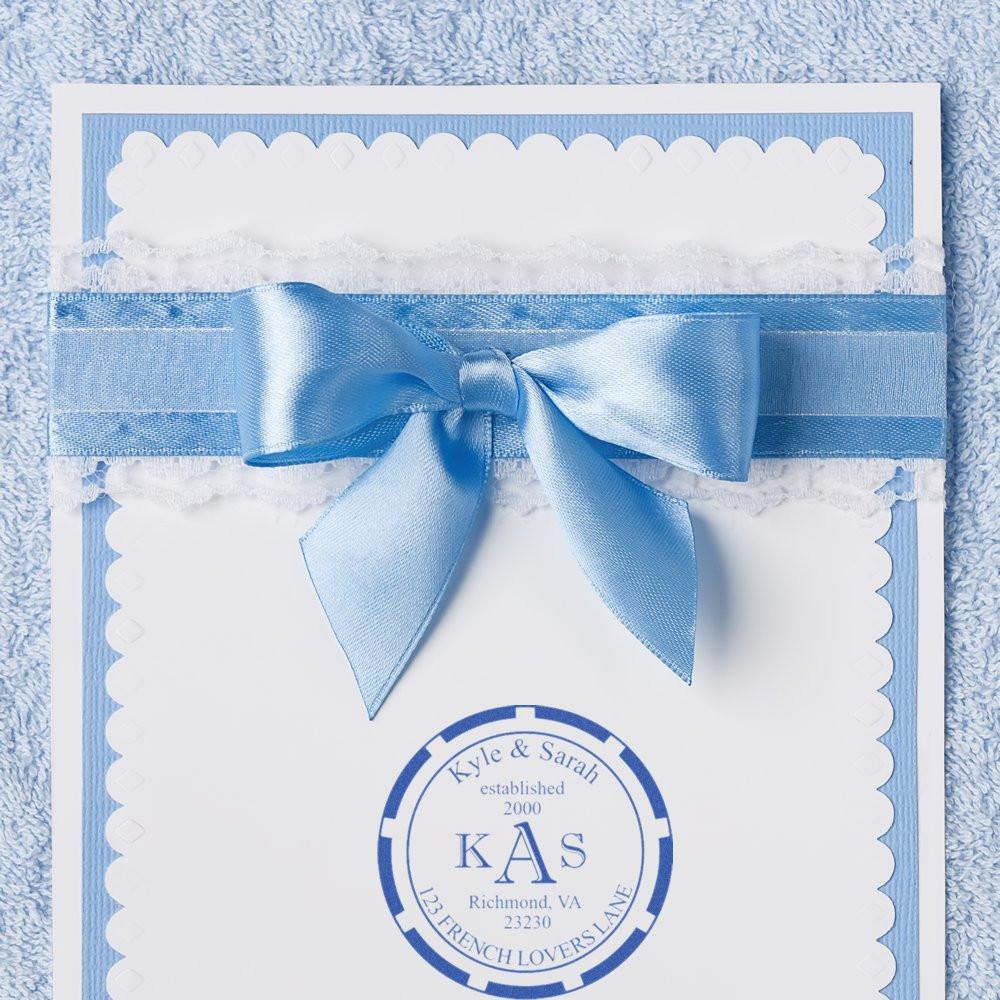 Custom wedding rubber stamp monogram seal on an elegant invitation card with a blue satin ribbon bow.