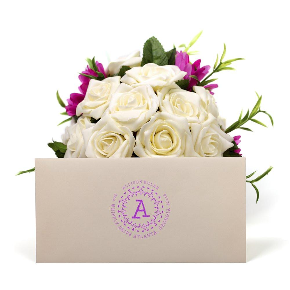 Personalized monogram return address rubber stamp on a wedding envelope with white roses and purple floral design.
