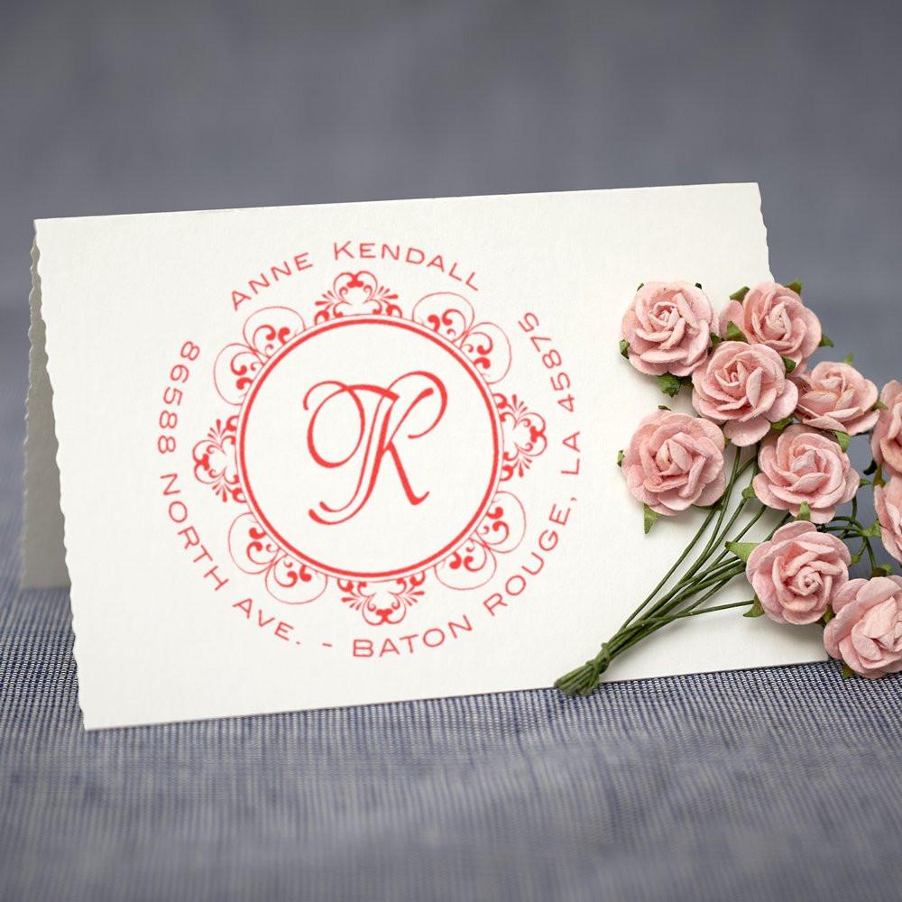 Custom return address rubber stamp with monogram and floral border, shown on paper with pink roses for wedding invitations.