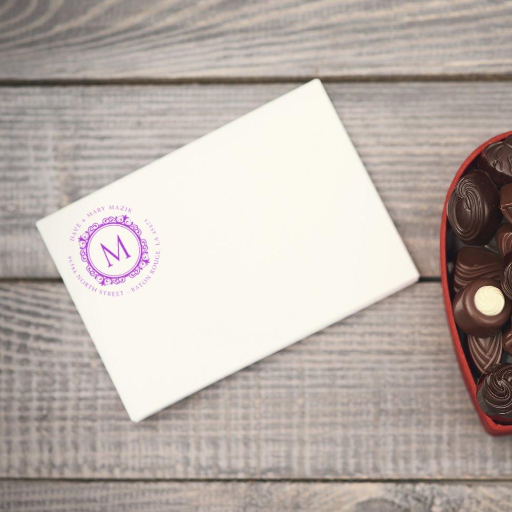 Custom rubber stamp monogram on cream envelope beside chocolates, showing branded stationery and gift packaging.