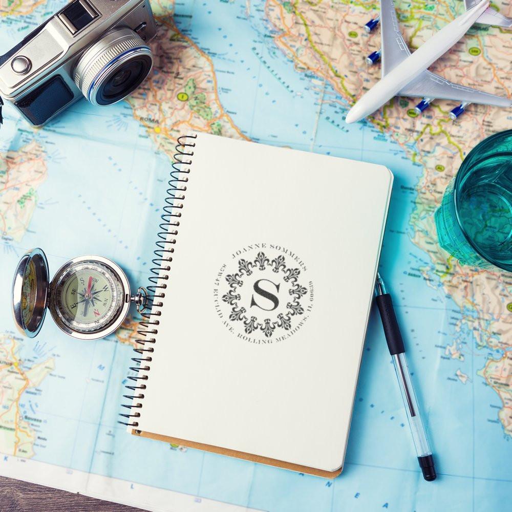 Personalized rubber stamp on spiral travel notebook with map, camera and compass for custom travel branding.