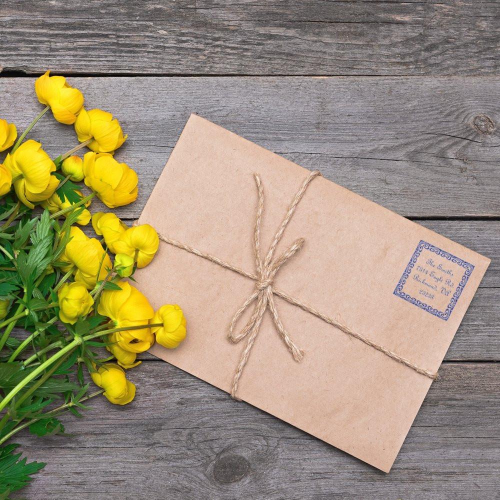 Handmade kraft paper gift with twine bow and greeting tag, beside yellow flowers on rustic wooden background.
