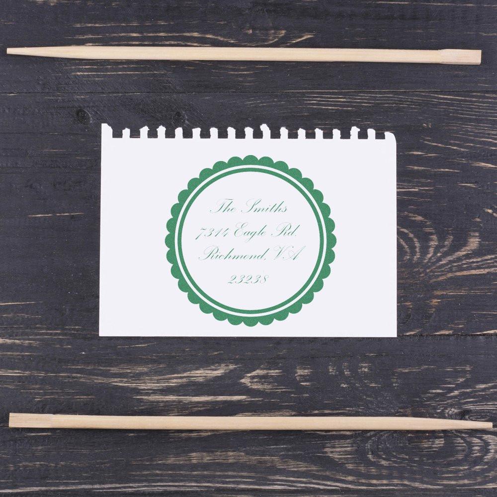 Custom rubber stamp impression with circular green address design on paper, shown with wooden stamp handles.