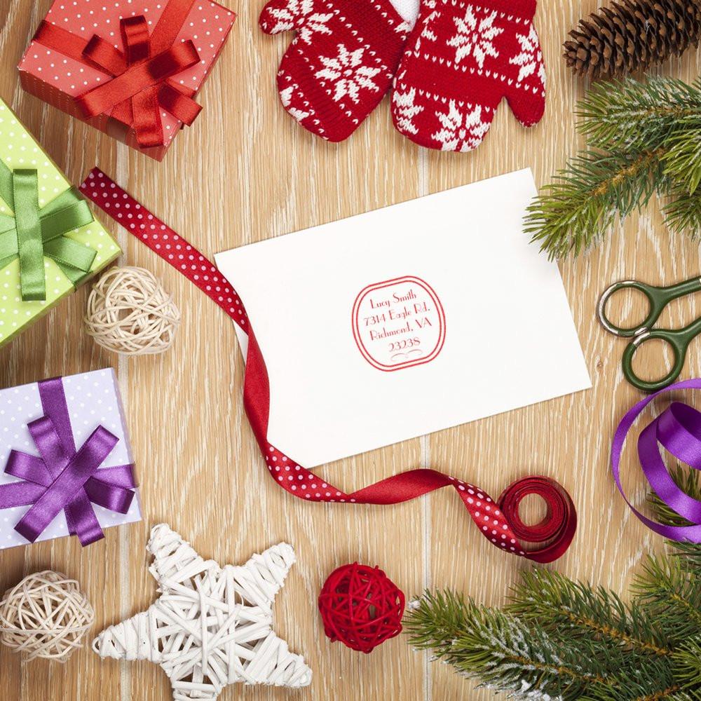 Custom return address rubber stamp on envelope in a holiday gift wrapping flat lay with ribbon, ornaments, and winter decor.
