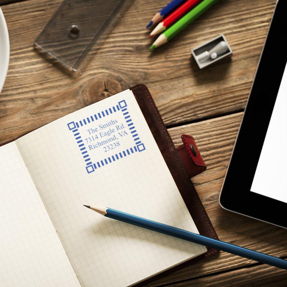 Handwritten mailing address label on notepad with pencils and stationery on wooden desk, representing address writing and delivery prep