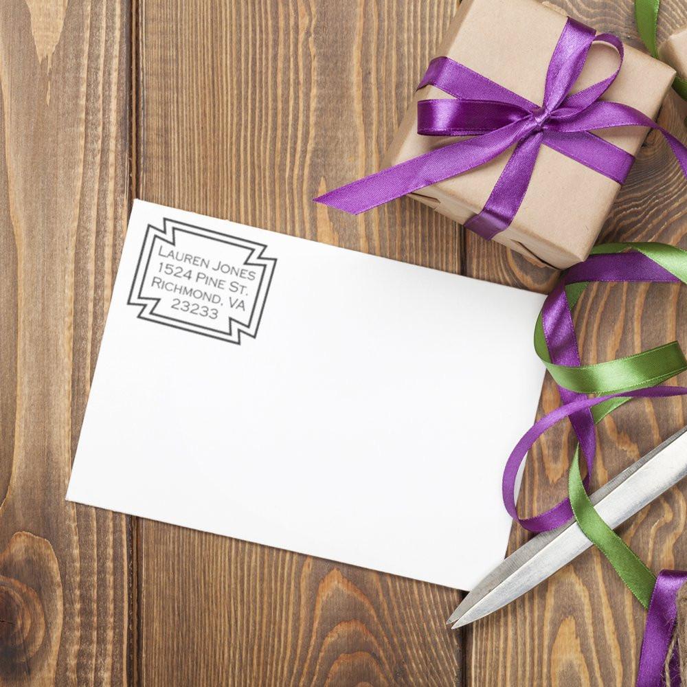 Custom return address rubber stamp on envelope beside gift box and ribbon, perfect for personalized mailing and packaging.