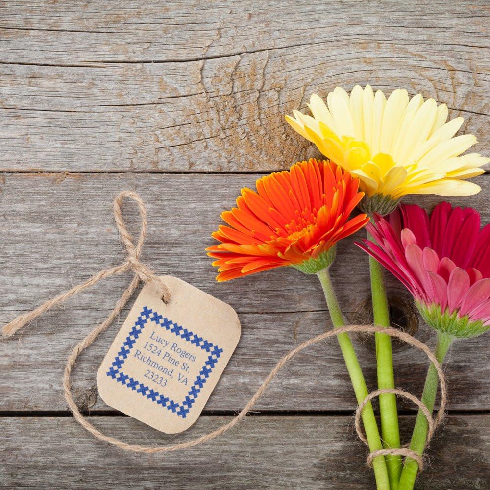 Custom address rubber stamp on a kraft tag with twine, styled with flowers for handmade packaging and gift labeling.
