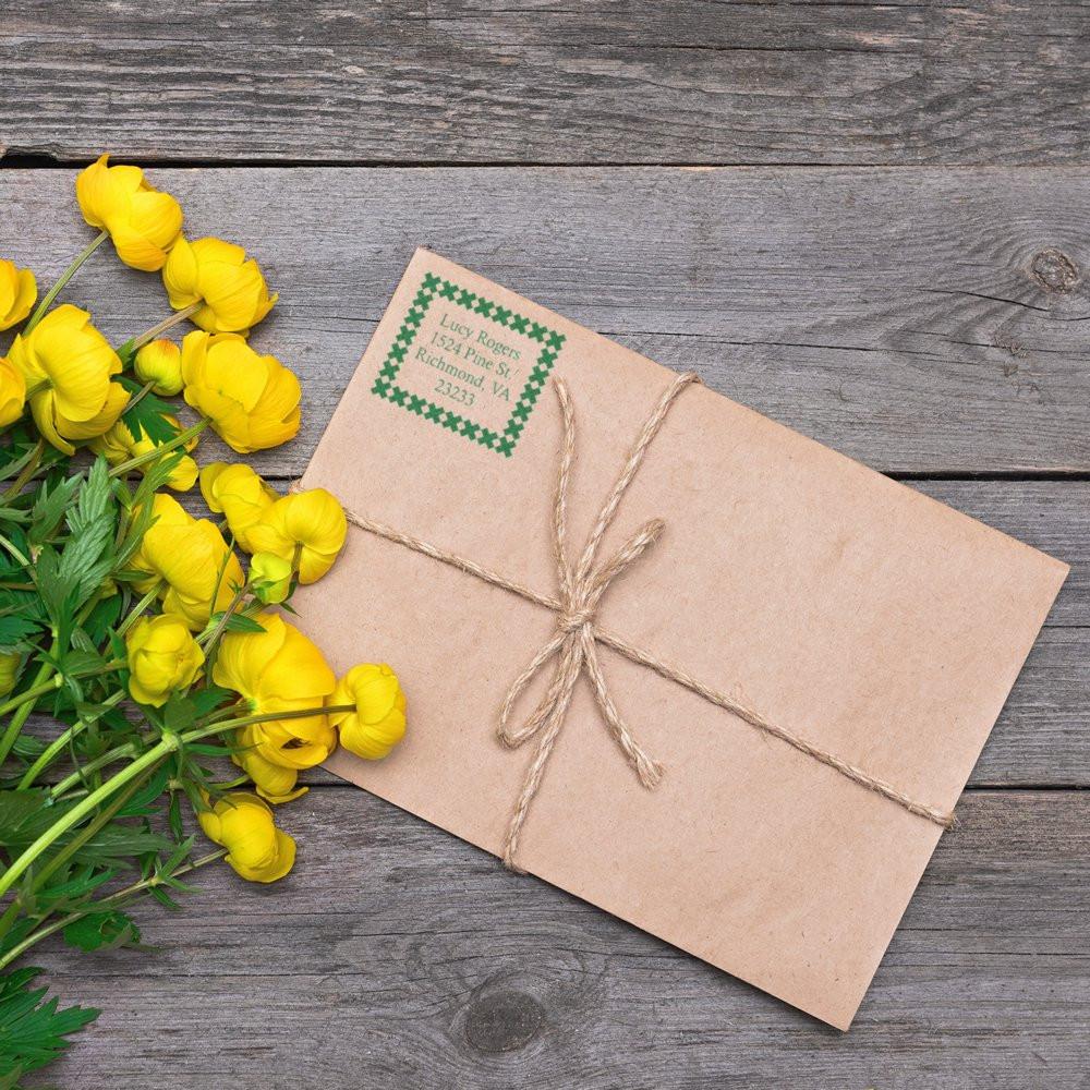Kraft envelope with custom return address rubber stamp, twine wrap, and yellow flowers on rustic wood.