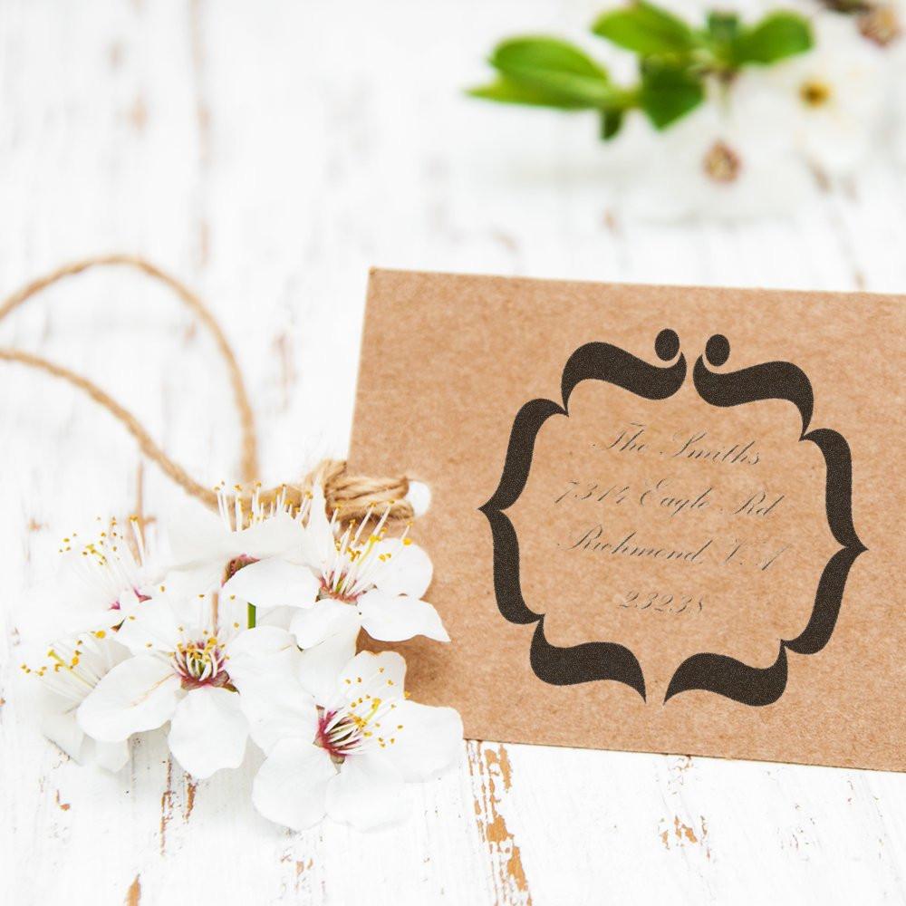 Custom return address rubber stamp on kraft wedding invitation card with twine and white flowers.