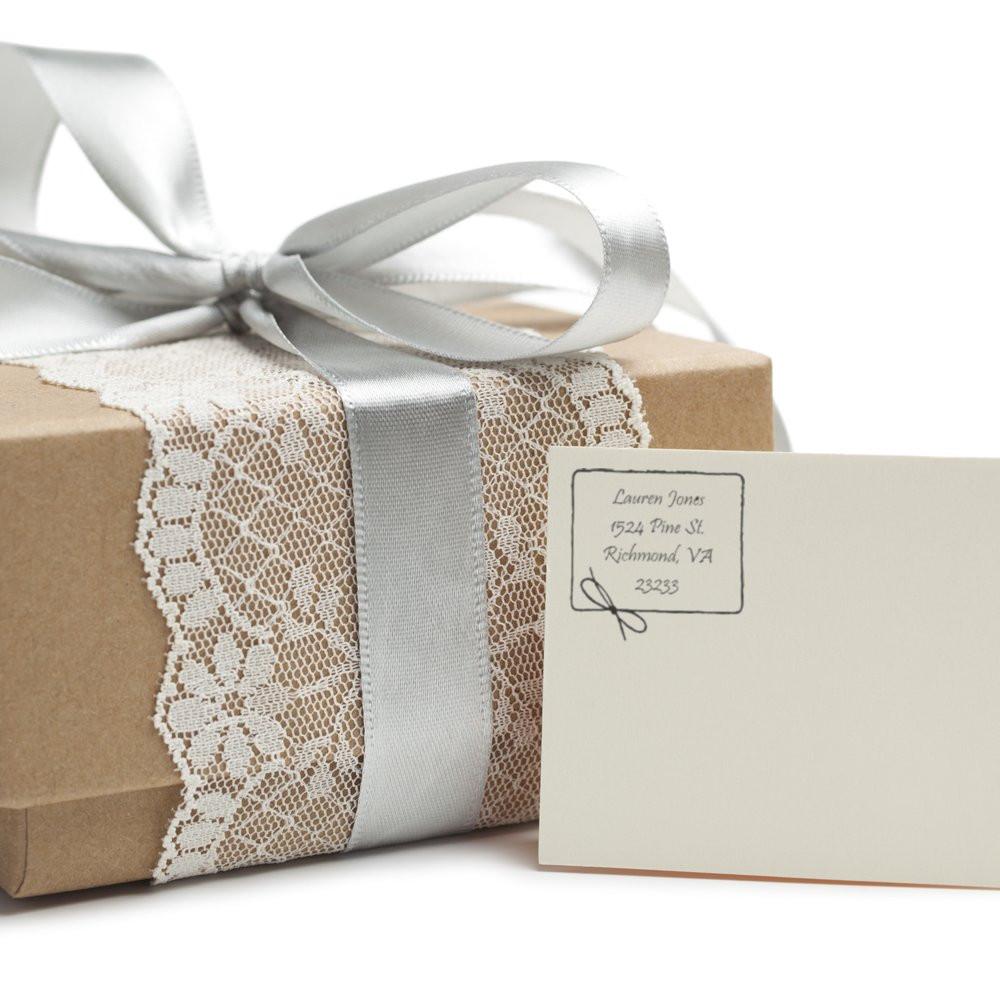 Custom rubber return address stamp on card beside wrapped gift with ribbon and lace.