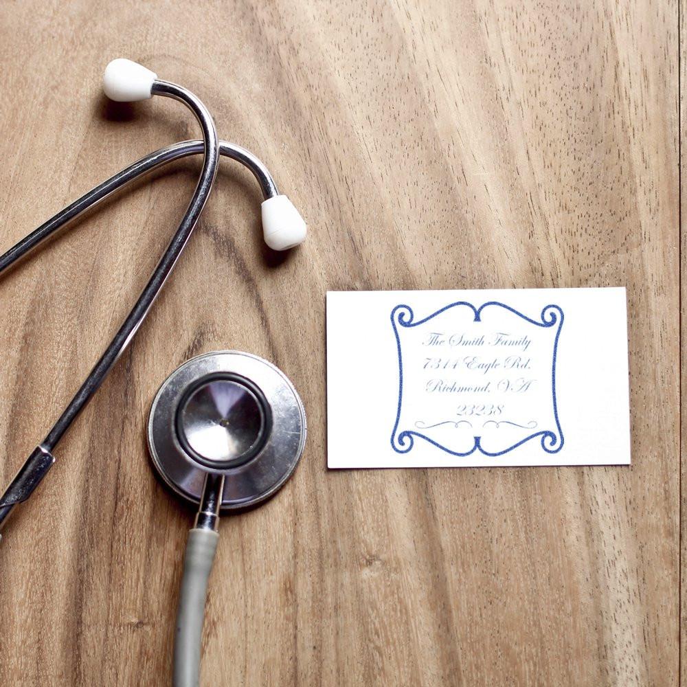 Custom rubber address stamp with decorative border on a card beside a stethoscope for personalized medical office mail.