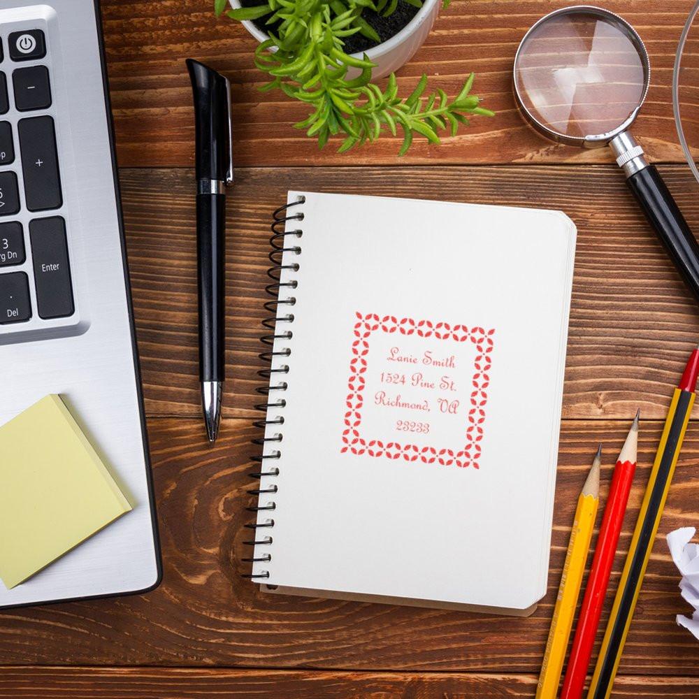 Custom return address rubber stamp on notebook with office supplies, showing a personalized mailing label design.