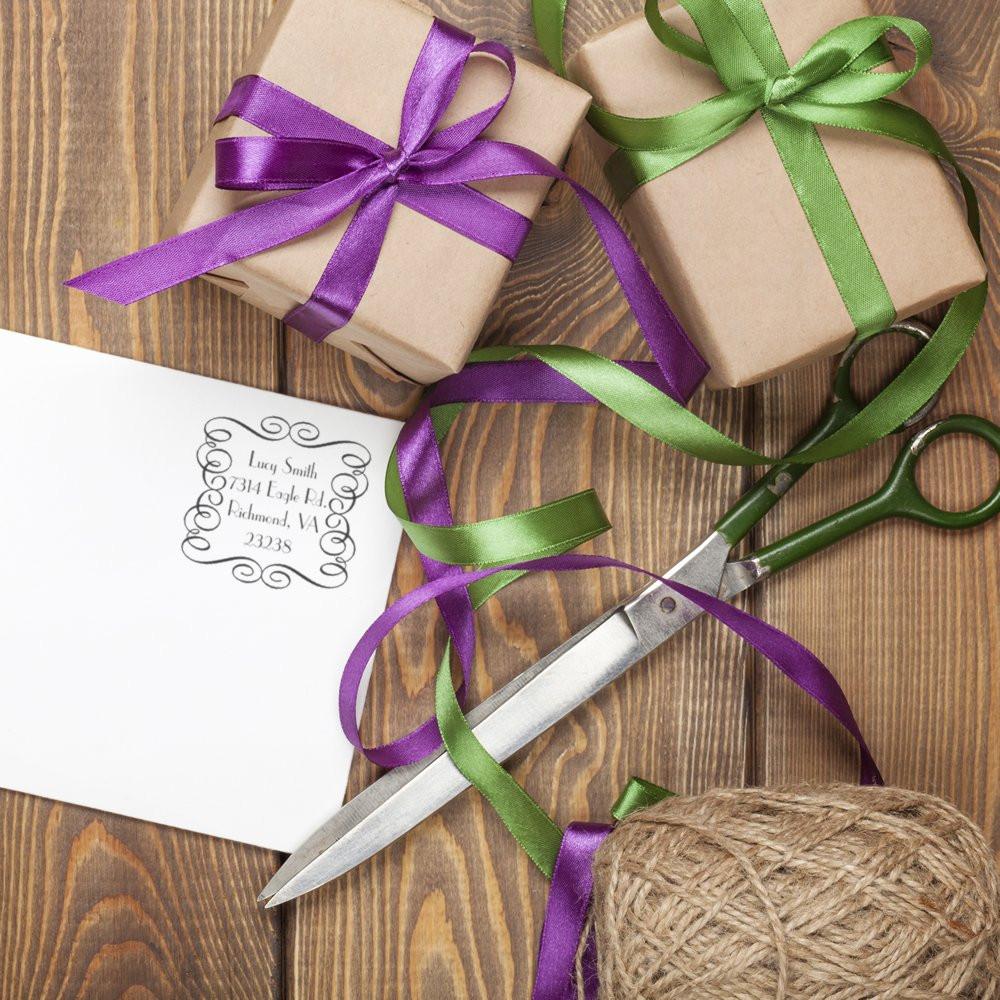 Custom address rubber stamp on holiday gift wrapping with ribbon, scissors, and wrapped presents for personalized packaging.