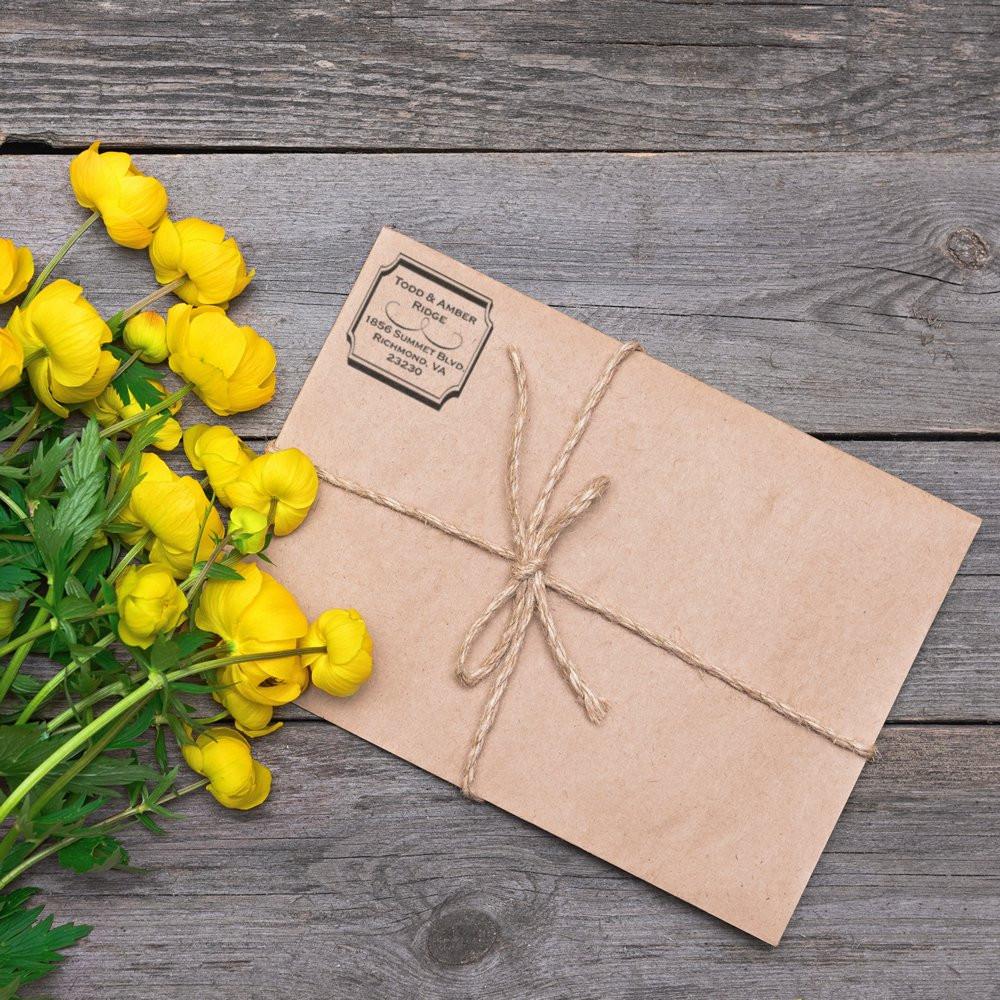 Personalized address rubber stamp on kraft envelope tied with twine, styled with yellow flowers for rustic wedding mailing.