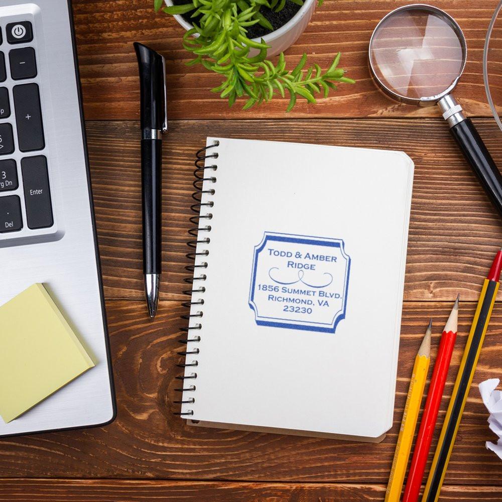 Custom address rubber stamp on notebook with office supplies, ideal for personalized stationery, wedding invites and branding.