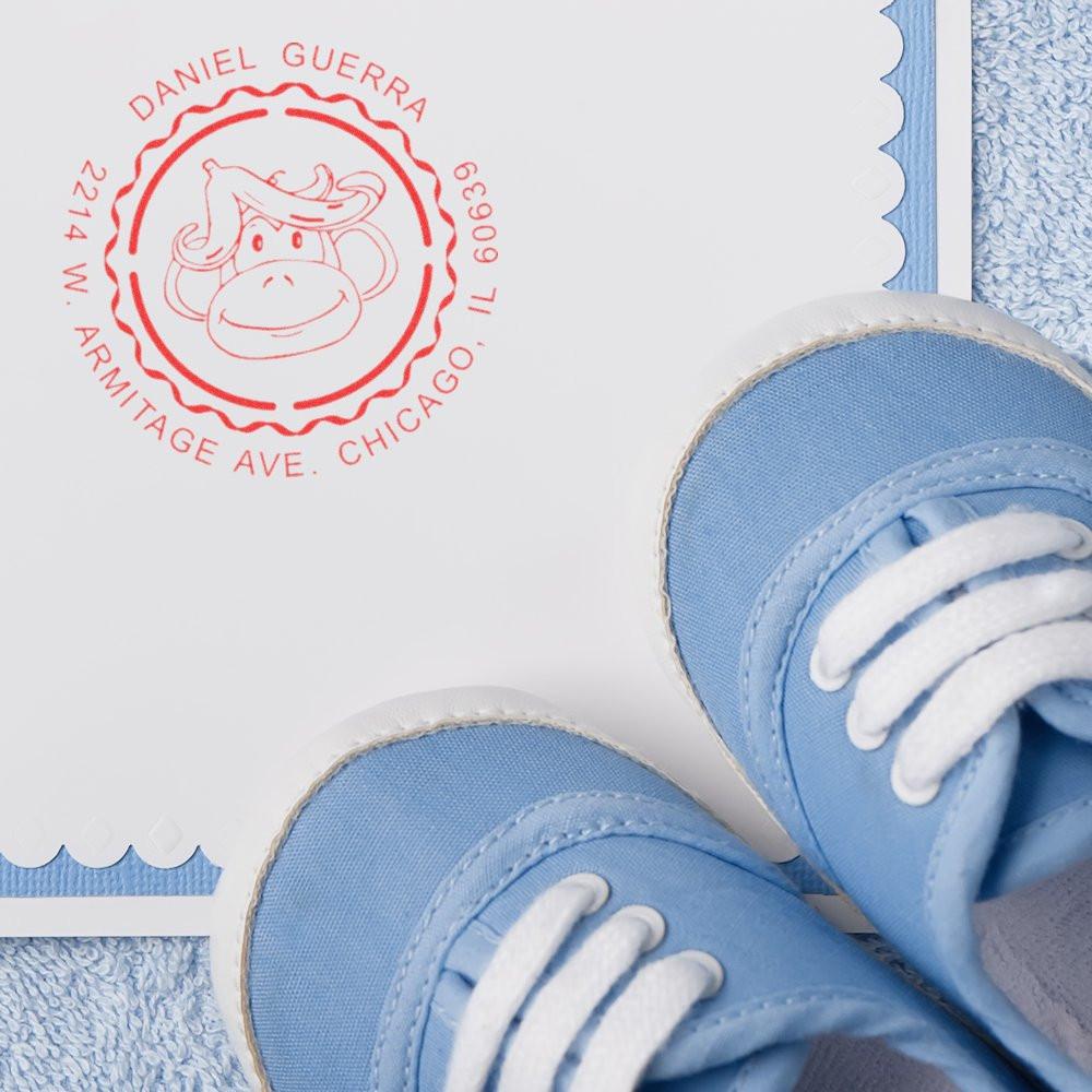 Custom return address rubber stamp with monkey logo imprint on stationery, beside baby blue baby shoes.