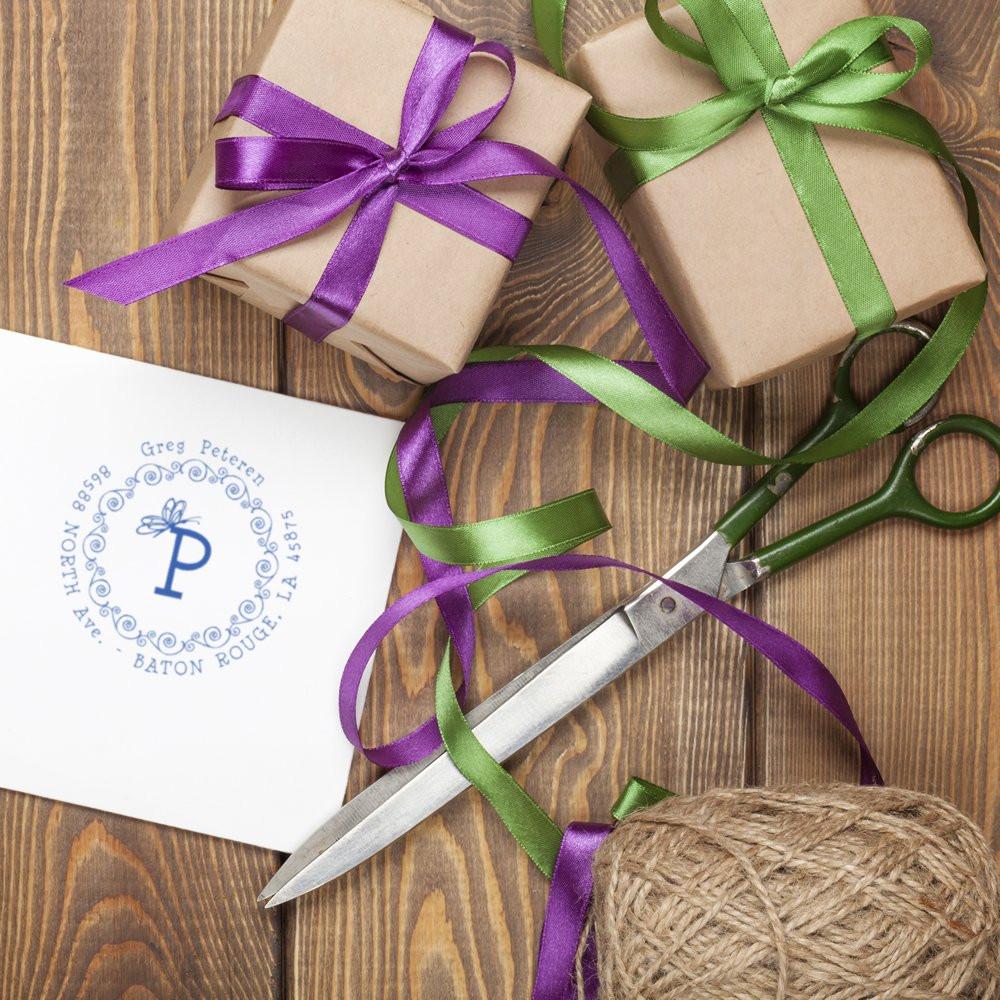 Personalized monogram return address rubber stamp on gift envelope with ribbon-wrapped presents, scissors, and twine.