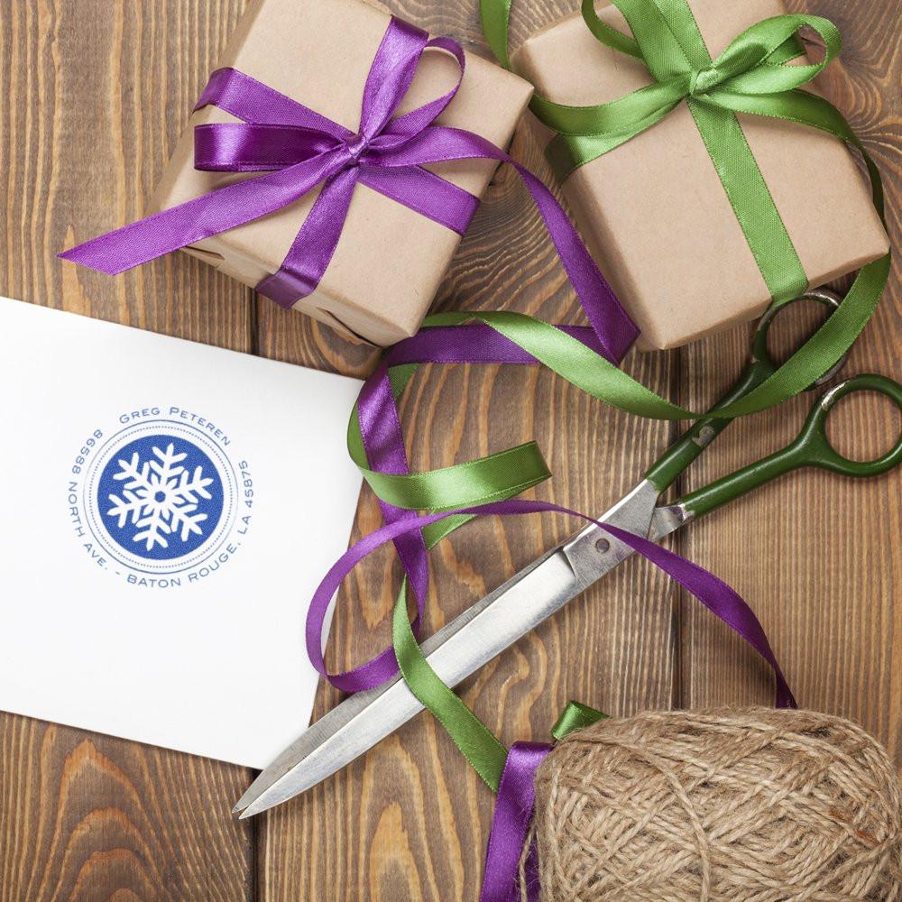 Winter holiday gift wrapping supplies with twine: purple and green ribboned presents, scissors, and snowflake delivery label on wood