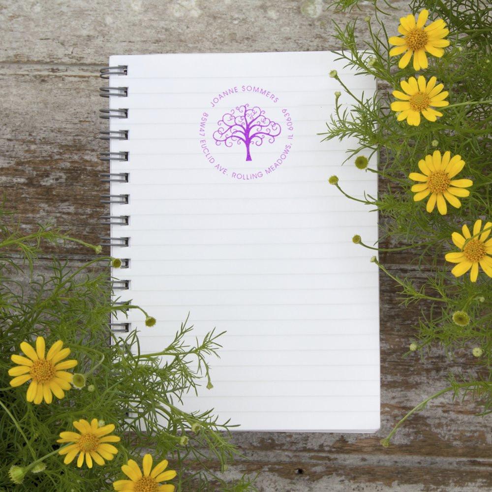 Custom rubber address stamp with tree logo on a notebook, ideal for personalized stationery and branding.