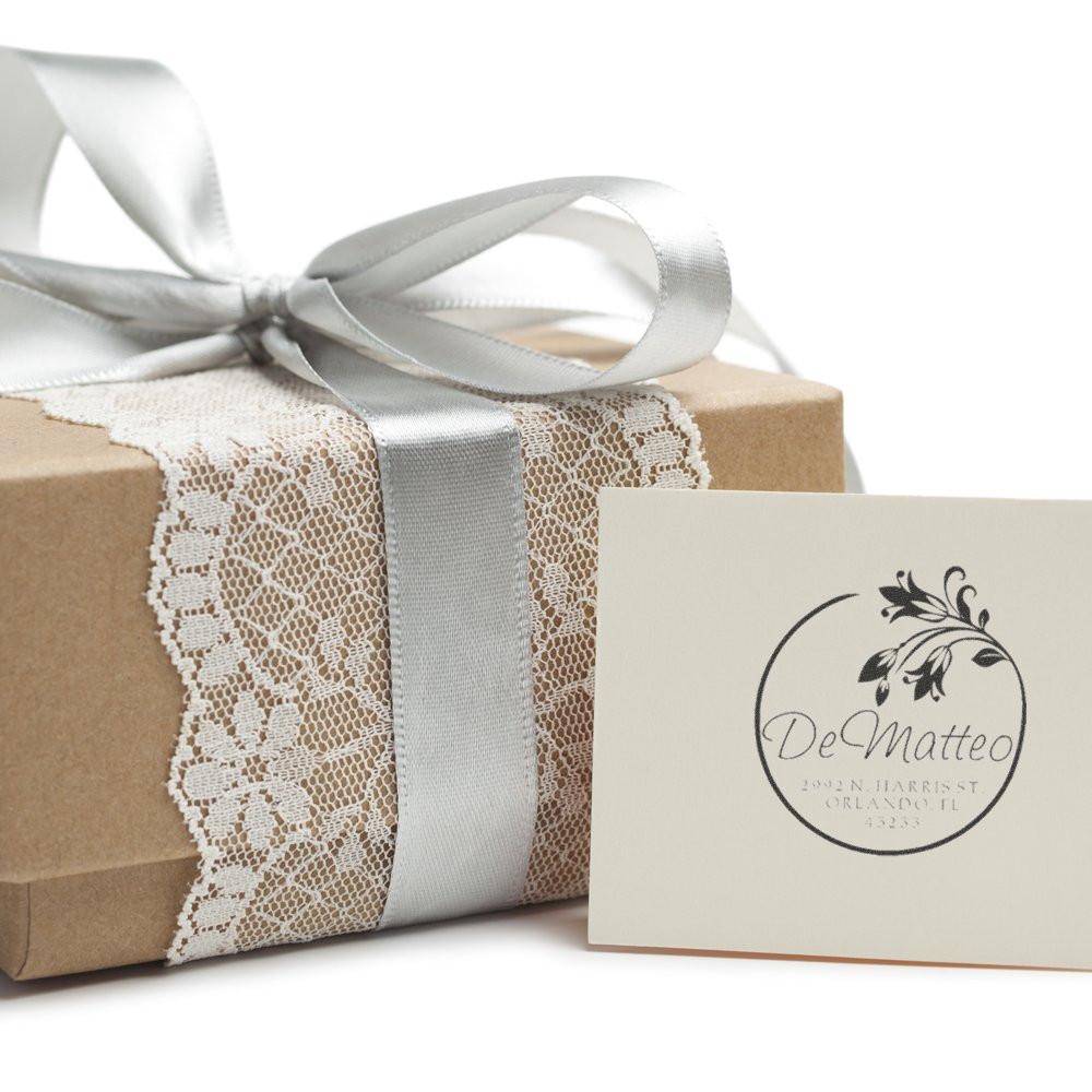 Custom rubber stamp return address card beside elegant gift wrapping with silver ribbon and lace for wedding packaging.