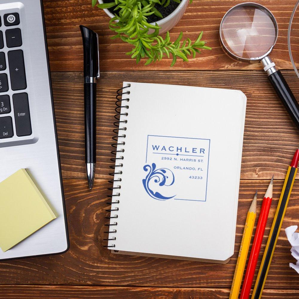 Custom address rubber stamp on notebook, displaying business logo and return address for office branding and mail.