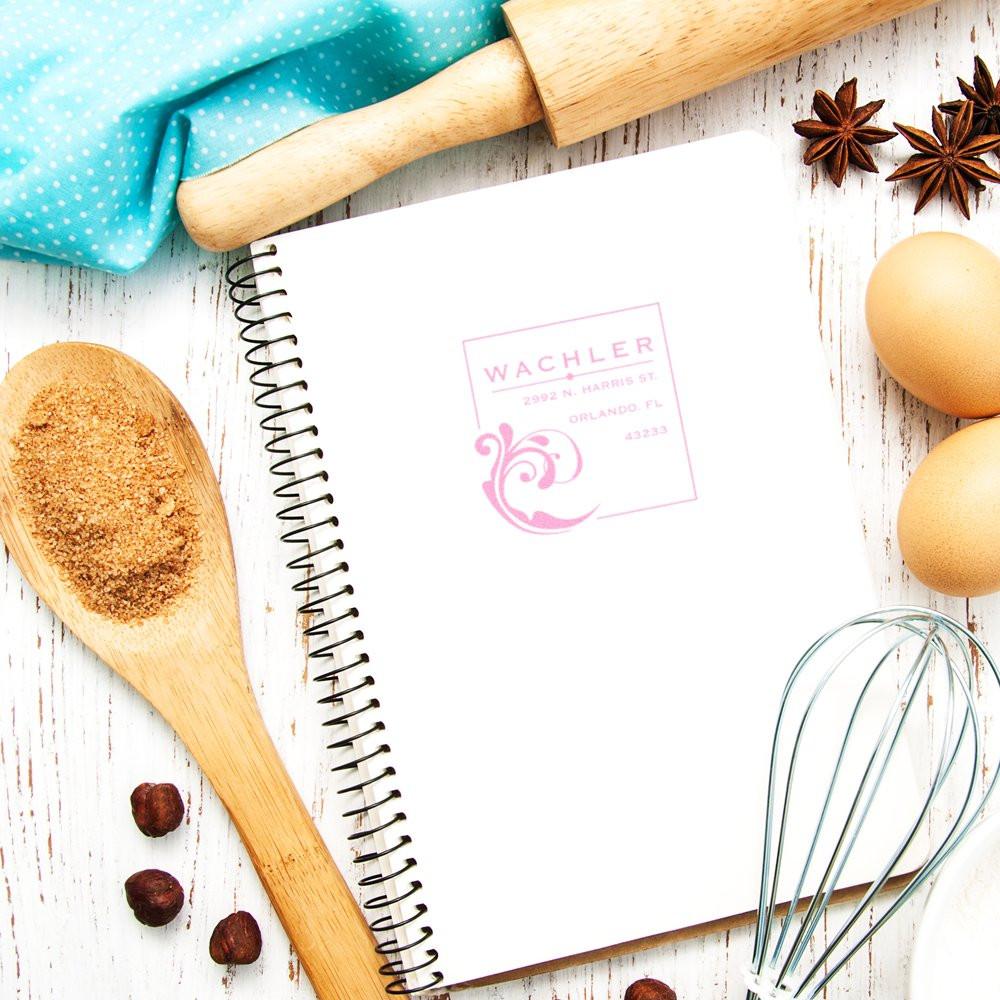 Personalized return address rubber stamp impression on a notebook, with baking props, for custom address labeling.